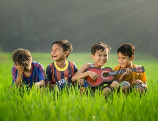 four boys laughing and sitting on grass during daytime
